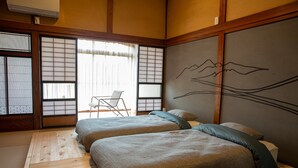 Een traditionele Japanse kamer met tatami vloeren, twee bedden met kussens, een schuifdeur met shoji schermen, en een muur met een berglandschap schilderij.