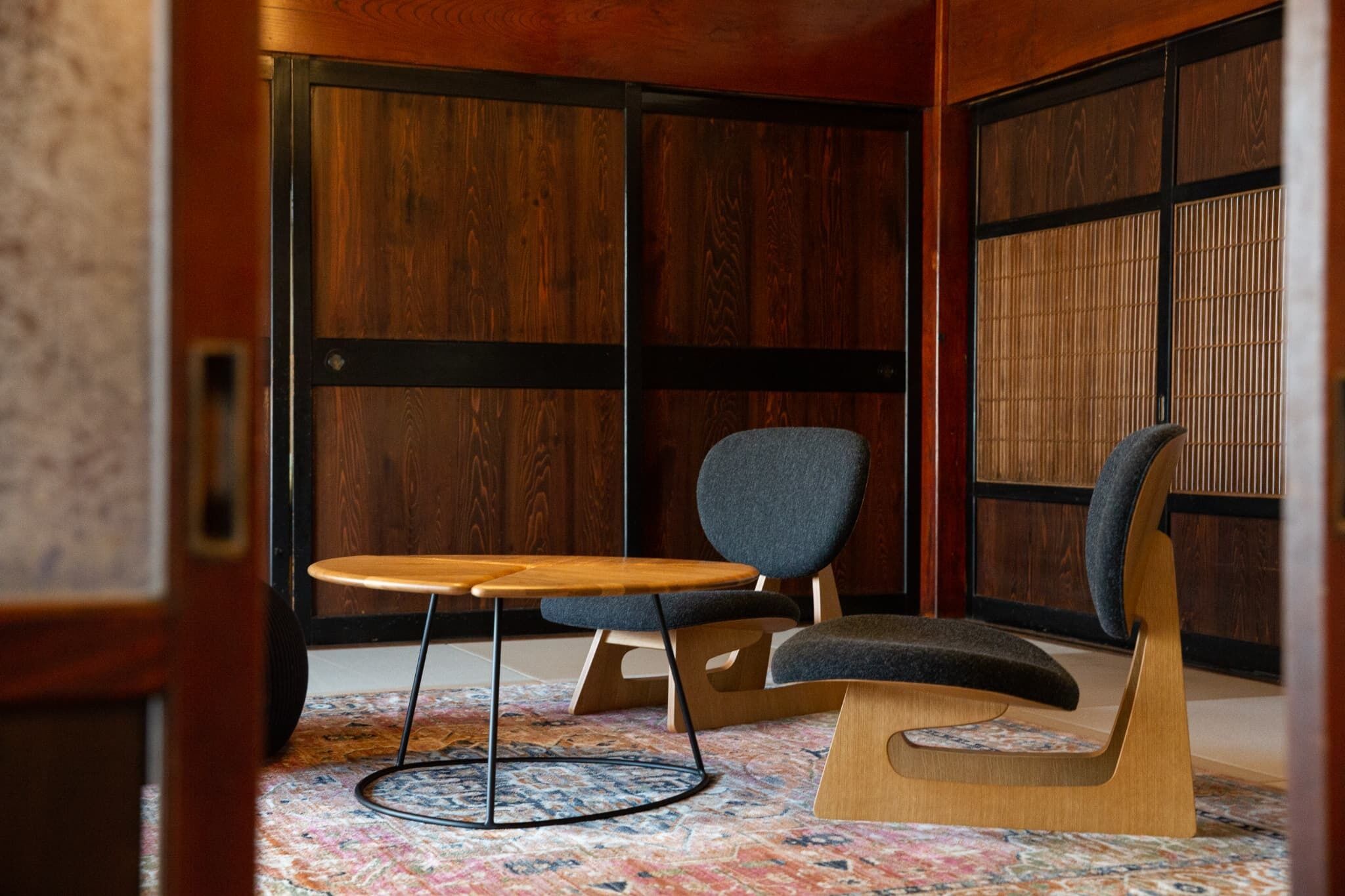 A room with a wooden floor, a round table with a chair, and a large window with wooden frames.