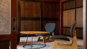 A room with a wooden floor, a round table with a chair, and a large window with wooden frames.