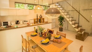A modern kitchen with white cabinets, a dining table set with yellow napkins, and a staircase with a unique design. - K's Casa Onna Village (Onna)