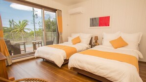 A hotel room with two beds, a balcony with a view of palm trees, and a wicker chair. - K's Casa Onna Village (Onna)