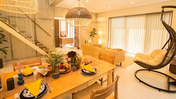 A dining area with a wooden table set for two, a hanging chair, and a staircase leading to another level. - K's Casa Onna Village (Onna)