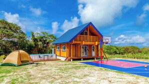 Una casa con techo azul, una cancha de baloncesto y una tienda de campaña.