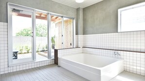 Ein modernes Badezimmer mit einer großen Badewanne, weiß geflieste Wände und einer Schiebeglastür, die auf eine Außenveranda führt.