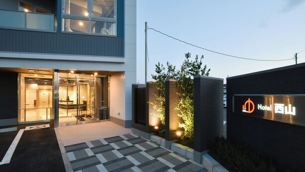 A modern hotel entrance with a glass facade, a checkered pathway, and a sign indicating the hotel name. - Hotel Nishiyama (Minamisoma)