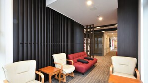 A hotel lobby with a seating area featuring a red sofa, two white armchairs, and a wooden table. - Hotel Nishiyama (Minamisoma)
