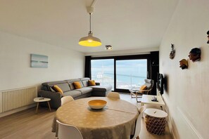 Ein modernes Wohnzimmer mit Esstisch, Sofa und Meerblick durch große Fenster.