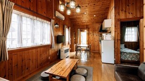 A wooden cabin interior with a dining area, kitchen, and a bed. - Canadian Village Montreal (Omachi)