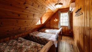 A small, wooden cabin room with two beds, a window, and a ceiling fan. - Canadian Village Montreal (Omachi)