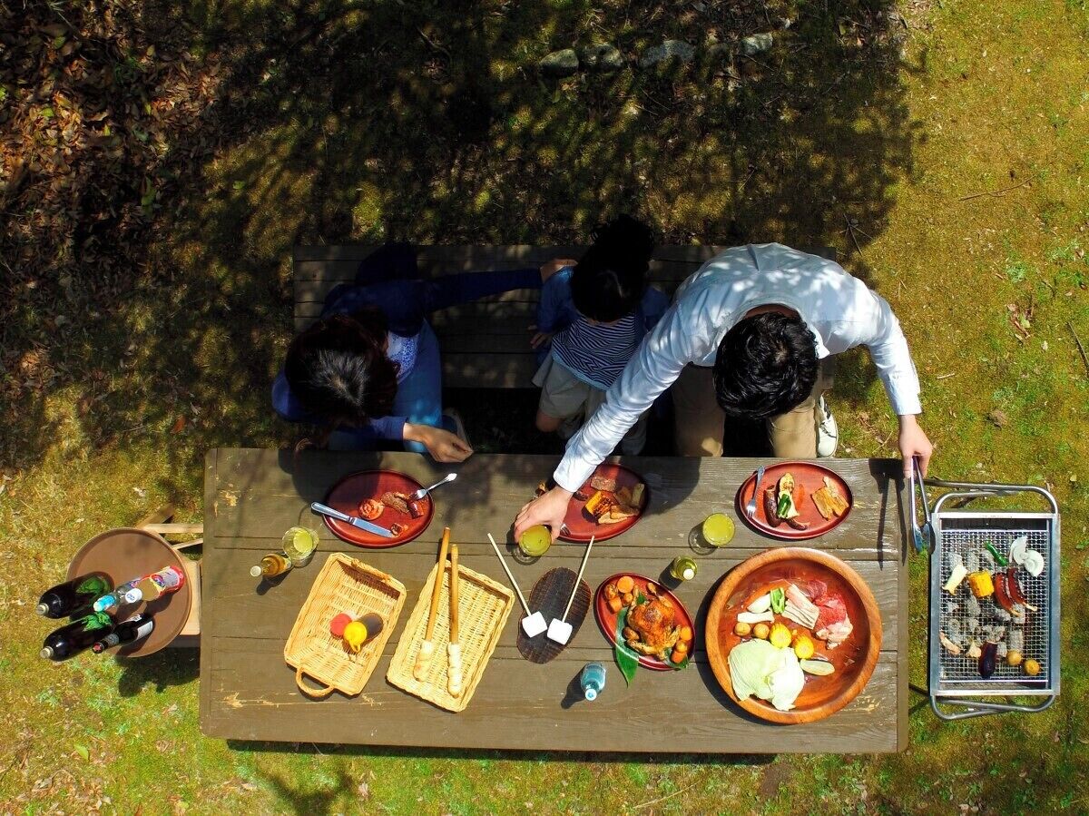 An outdoor dining area with a wooden table set for a meal, surrounded by greenery.