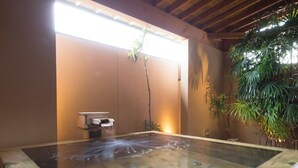 A hot spring bath with a wooden edge, a small table, and potted plants. - Ryokan Kobushi (Nantan)