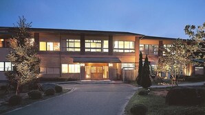 A modern two-story building with a well-lit entrance and a paved driveway. - Ryokan Kobushi (Nantan)