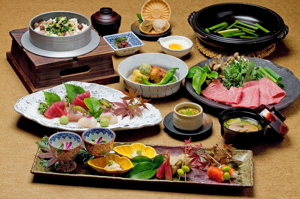 A variety of dishes and food items, including sushi, sashimi, and a hot pot, arranged on a table.