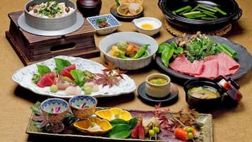 A variety of dishes and food items, including sushi, sashimi, and a hot pot, arranged on a table.