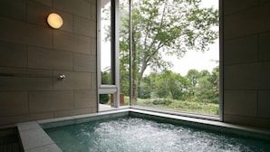 A spa area with a hot tub, a window with a view of greenery, and a wall-mounted light fixture. - Kusatsu Onsen Hotel Kurbio (Kusatsu)