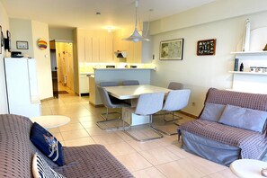 A modern living room with a sofa, a dining table with chairs, and a kitchen area in the background. - Beachfront apartment in Nieuwpoort (NIEUWPOORT)