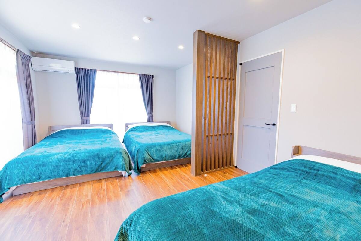 Une chambre d’hôtel avec deux lits, un plancher en bois, une fenêtre avec des rideaux et une porte.