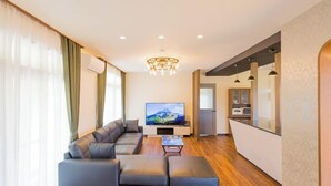 En moderne stue med en modulsofa, et fladskærms TV og et spiseområde med et køkken i baggrunden.