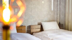 Een slaapkamer met twee bedden, houten nachtkastjes en een betonnen muur.