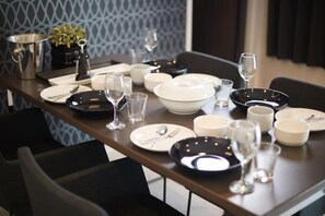 A dining table set with plates, bowls, glasses, and cutlery, with a plant and a metal container in the background. - Sesoko Villa (Motobu)