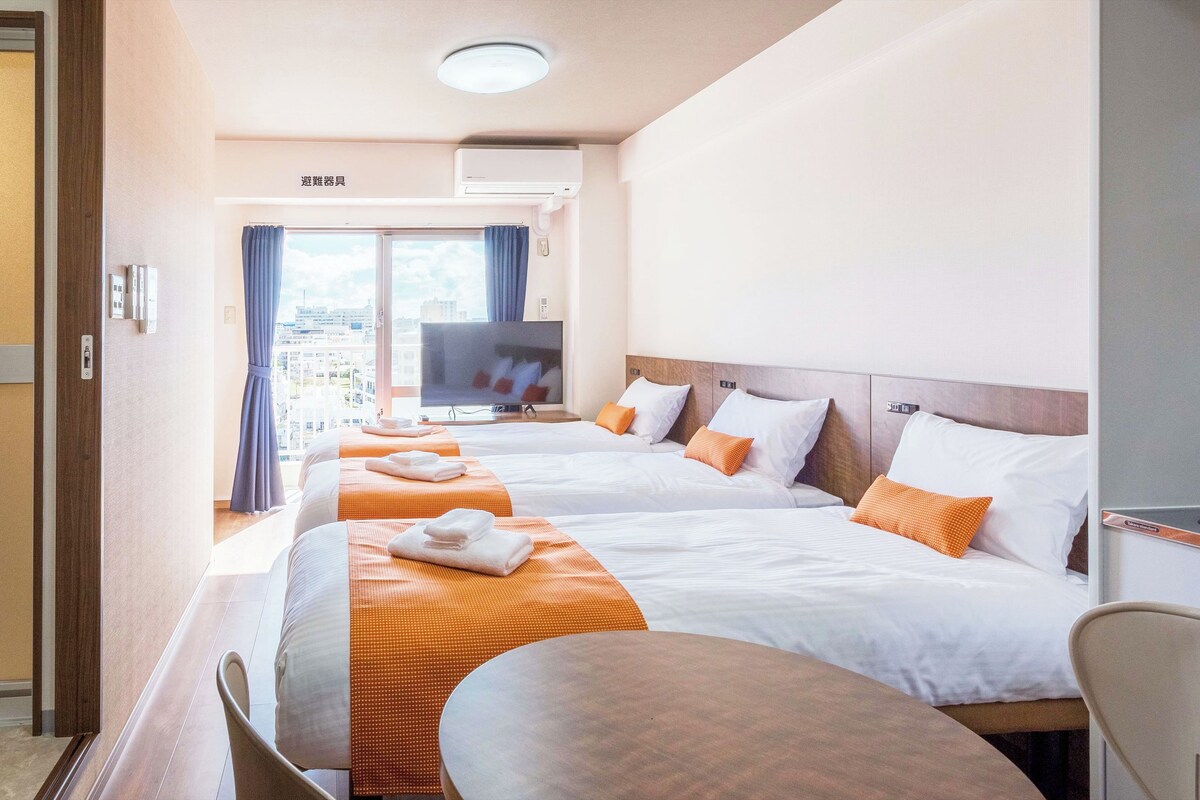Quarto de hotel com duas camas, televisão, cozinha compacta e vista para a cidade.
