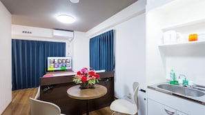 A compact hotel room with a bed, a small table with a vase of flowers, a desk with a computer, a chair, a sink, and a window with curtains. - Kariyushi Condominium Resort Naha Ryujin Hotel Ukishima (Naha)