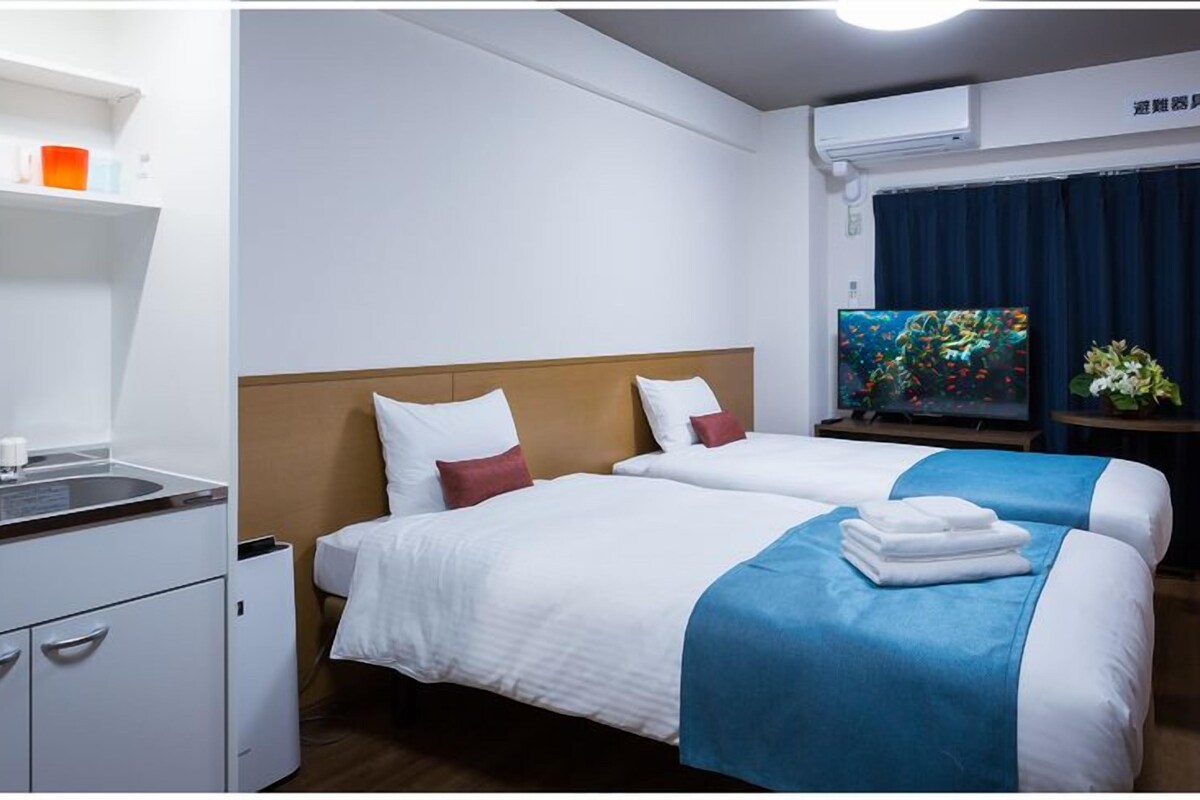 Quarto de hotel com duas camas, televisão, pia e minibar.