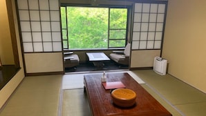 A traditional Japanese room with tatami flooring, a wooden table, and a view of greenery outside. - Yurakutei (Kamiamakusa)