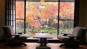 A room with a view of autumn foliage through large windows, two chairs, a small table, and a wooden floor. - Yurakutei (Kamiamakusa)