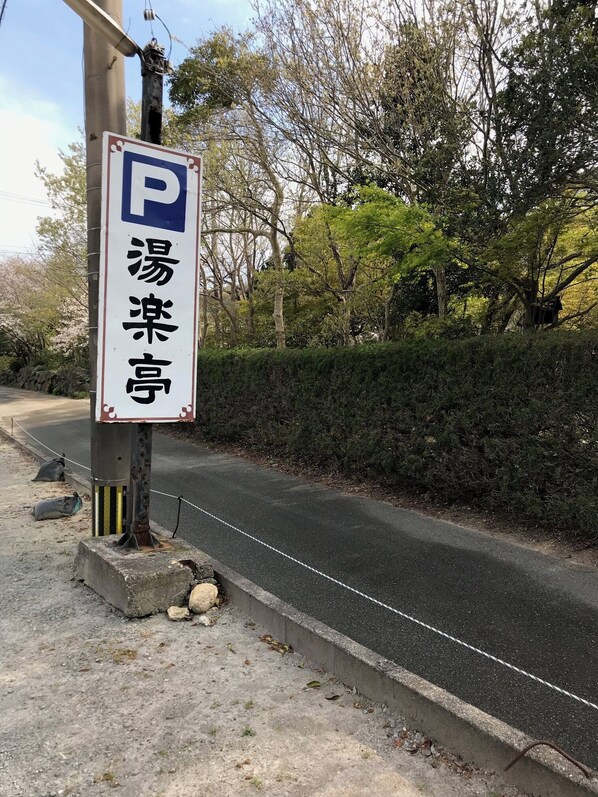 A parking sign with Japanese characters, a concrete barrier, and a road with trees and bushes.