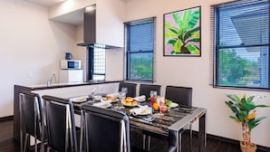 Un espace de salle à manger moderne avec une longue table, des chaises noires et une cuisine en arrière-plan.