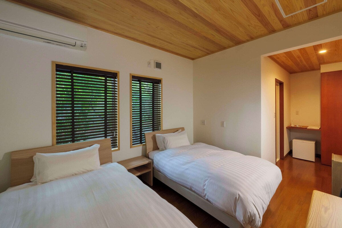 A room with two beds, wooden ceiling, and a desk with a lamp.