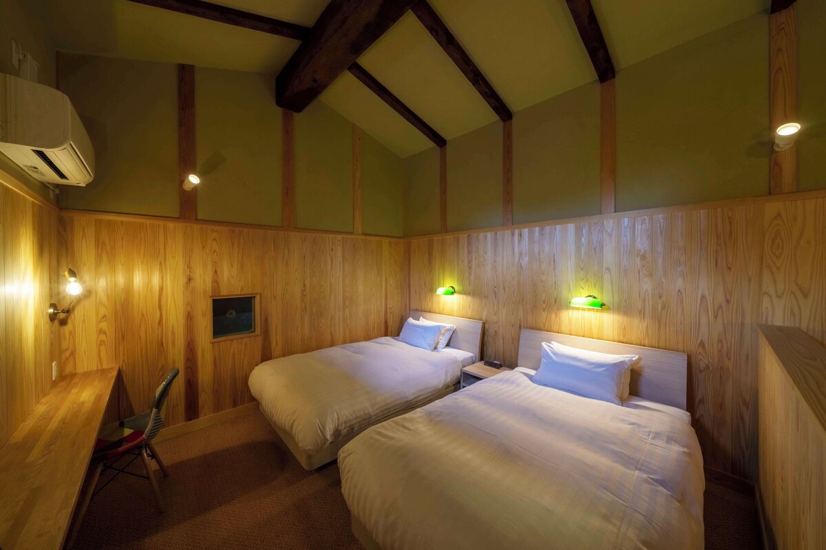 A room with two beds, wooden walls, and a desk with a chair.