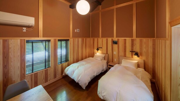 A room with two beds, a table, and a ceiling light. - Guesthouse Obuse (Obuse)