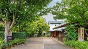 A traditional Japanese building with a tiled roof, surrounded by lush greenery and a paved pathway leading to it. - Guesthouse Obuse (Obuse)