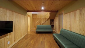 A wooden-paneled room with a green sofa, a flat-screen TV, and a staircase leading to another level. - Guesthouse Obuse (Obuse)