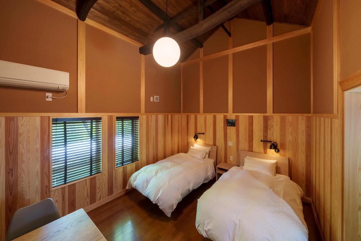 A room with two beds, wooden walls, a ceiling fan, and a table.