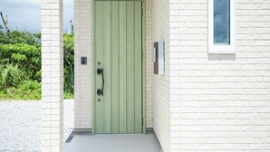 A green door with a handle, a window, and a brick wall. - Makai Green (Nakijin)
