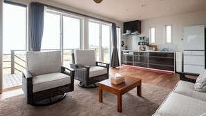A spacious living area with a large window, a ceiling fan, and a kitchen area with modern appliances. - Makai Green (Nakijin)