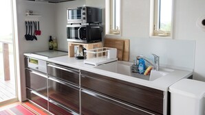 A modern kitchen with a stainless steel range hood, double microwave, and a wooden cutting board on the counter. - Makai Green (Nakijin)