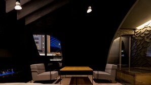 Een moderne kamer met een gebogen plafond, een houten tafel, twee fauteuils en een groot raam met uitzicht op de stadsgezicht.