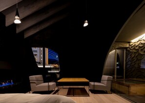 A modern room with a curved ceiling, a wooden table, two armchairs, and a large window offering a view of the cityscape. - Kusatsu Onsen Kimuraya (Kusatsu)