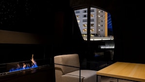 Een modern interieur met een open haard, een stoel, een tafel en uitzicht op een gebouw door een raam.