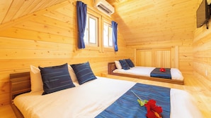 Een houten hut met twee bedden, een plafondventilator en een tv aan de wand.