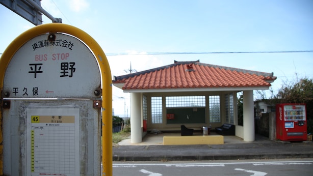 Een bushalte met een beschutte overkapping, een Coca-Cola automaat en een bord met Japanse tekst.