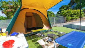 Een Coleman tent staat opgezet op een grasveld, met een opklapbare tafel en kookspullen.