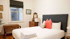 A neatly made bed with white linens, a wooden bench, a dresser with a mirror, and a window with a dark valance. - Spacious 4-Bed Home in Central Tenterfield (Tenterfield)