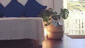 Une chambre à coucher avec un lit, des oreillers bleus, une plante en pot et une vue sur des palmiers par la fenêtre.