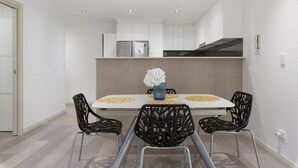 Een moderne eetruimte met een rechthoekige tafel, vier zwarte stoelen en een vaas met witte bloemen.