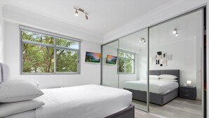 Een moderne slaapkamer met een groot bed, een inloopkast en uitzicht op bomen door de ramen.